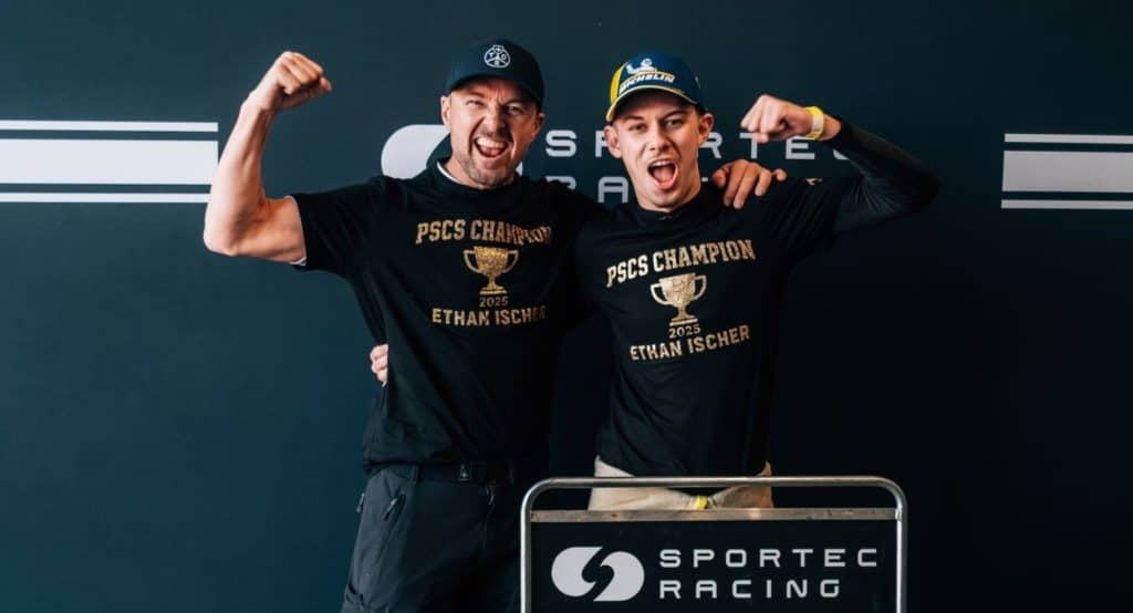 Two race winners celebrating at the podium with trophies and team shirts.